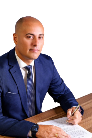 Retrato de Sérgio Augusto Cardozo, advogado, de terno azul-marinho, sentado à mesa de trabalho, com uma caneta sobre um documento